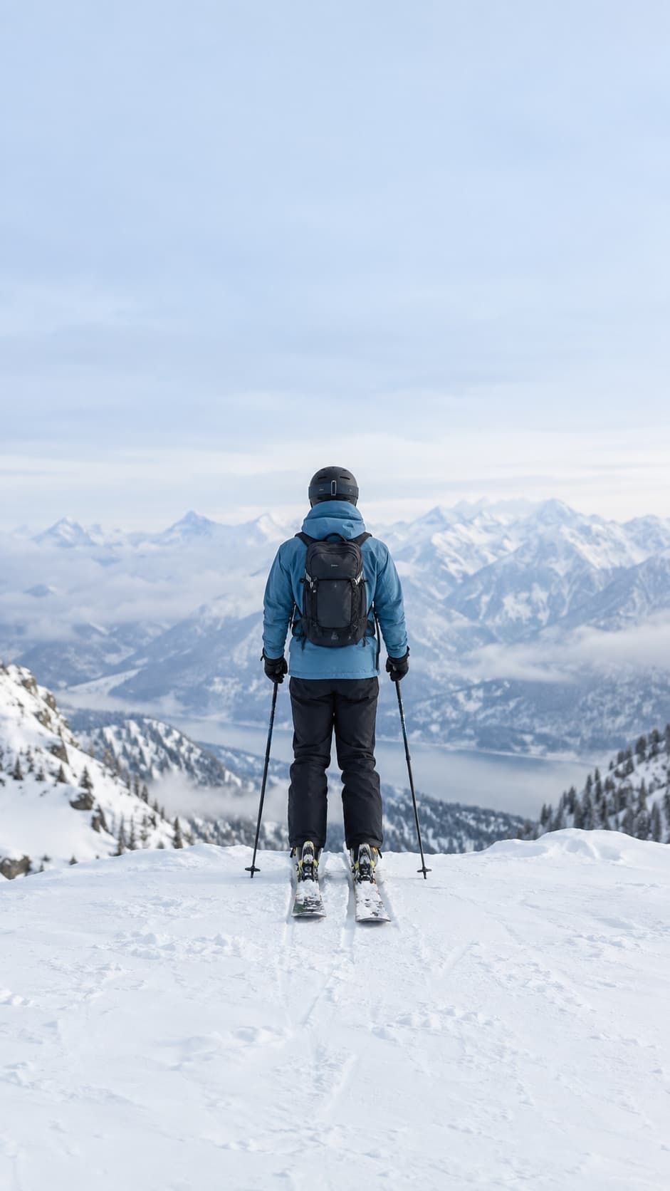 A skier in a blue jacket looking out over snowy mountains